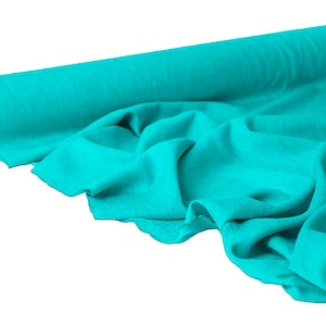 May include: A roll of turquoise fabric, partially unrolled to reveal the soft texture. The fabric is a solid color, with visible folds and creases. The roll is made of a cardboard core.