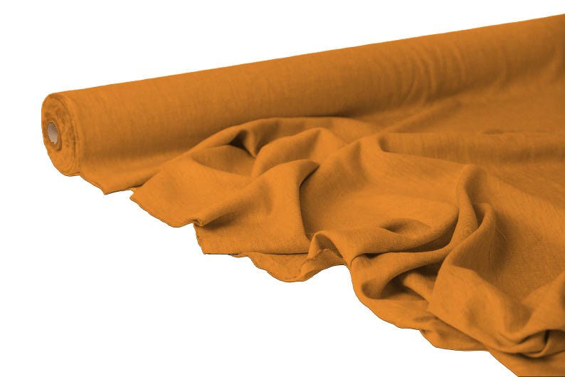 May include: A roll of mustard-colored fabric with a soft, flowing drape. The fabric is partially unrolled, revealing the texture and folds of the material. The background is plain white.