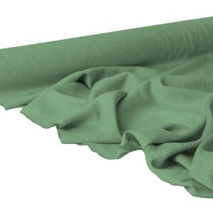 May include: A roll of sage green fabric with a soft, flowing texture. The fabric is partially unrolled, revealing its drape and the texture of the material. The roll has a cardboard core.