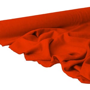 May include: A roll of vibrant orange fabric, partially unrolled to reveal soft folds. The fabric is a solid color, with a smooth texture. The roll is positioned on the left side of the image, with the unrolled fabric cascading towards the right.