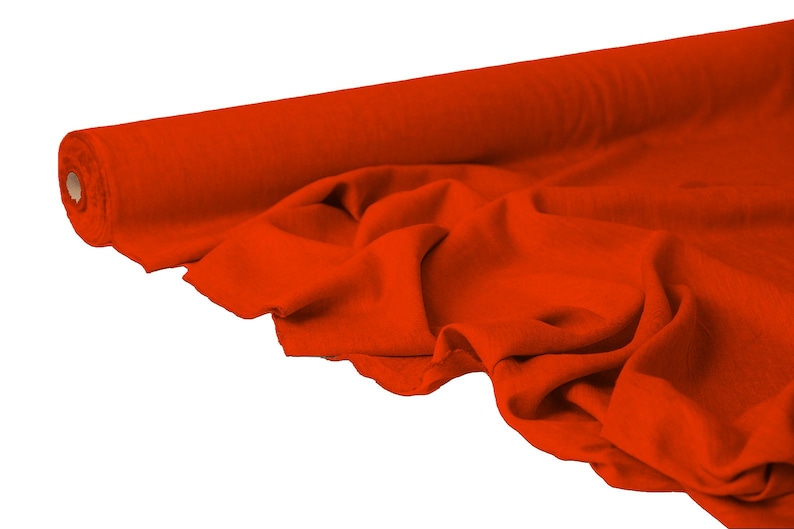 May include: A roll of vibrant orange fabric, partially unrolled to reveal soft folds. The fabric is a solid color, with a smooth texture. The roll is positioned on the left side of the image, with the unrolled fabric cascading towards the right.