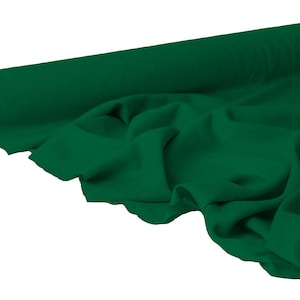 May include: A roll of emerald green fabric, partially unrolled to reveal the soft texture. The fabric is draped, showing folds and shadows. The roll is cylindrical with a cardboard core.
