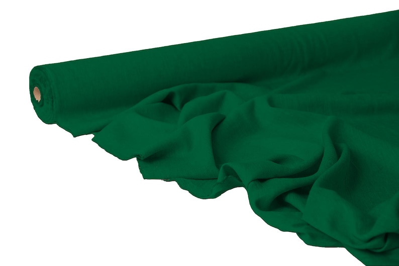 May include: A roll of emerald green fabric, partially unrolled to reveal the soft texture. The fabric is draped, showing folds and shadows. The roll is cylindrical with a cardboard core.