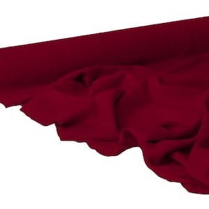May include: A roll of deep red fabric, partially unrolled to reveal soft folds. The fabric is a solid color, with a smooth texture. The roll is visible on the left side, showing the end of the material.
