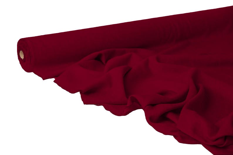 May include: A roll of deep red fabric, partially unrolled to reveal soft folds. The fabric is a solid color, with a smooth texture. The roll is visible on the left side, showing the end of the material.