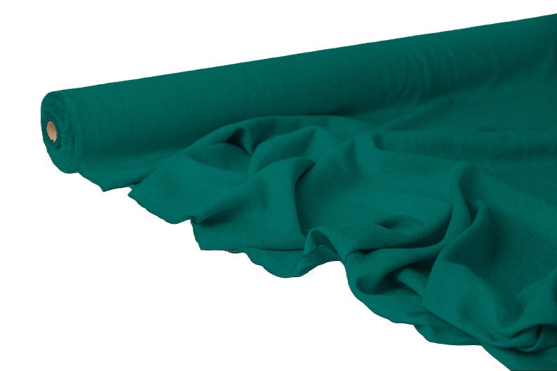 May include: A roll of teal fabric, partially unrolled to reveal the soft texture. The fabric is a solid teal color, with visible folds and drapes. The roll is positioned on the left side of the image, with the unrolled fabric cascading towards the right.