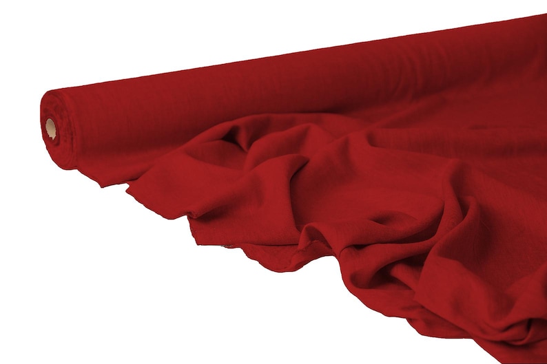 May include: A roll of vibrant red fabric, partially unrolled to reveal the soft texture. The fabric is draped, showing its folds and the way it catches the light. The roll is on the left side of the image, with the fabric extending to the right.