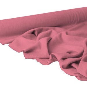 May include: A roll of dusty rose fabric, partially unrolled to reveal soft folds. The fabric is a solid color, with a slightly textured appearance. The roll is positioned on the left side of the image, with the fabric cascading towards the right.