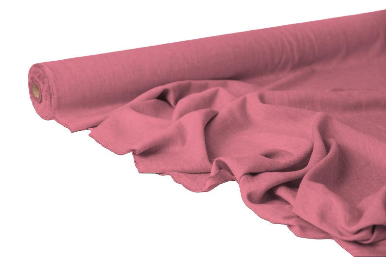May include: A roll of dusty rose fabric, partially unrolled to reveal soft folds. The fabric is a solid color, with a slightly textured appearance. The roll is positioned on the left side of the image, with the fabric cascading towards the right.