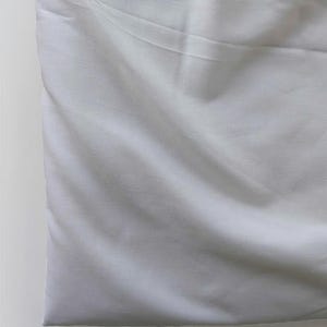 May include: A folded, white fabric with soft folds and subtle shadows. The material appears to be smooth and possibly cotton or linen, suggesting bedding or clothing.