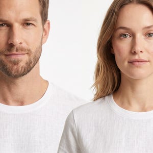 May include: Two individuals are shown wearing plain white crew neck t-shirts. The shirts feature a standard short-sleeve design with a simple round neckline, constructed from a lightweight fabric with a visible, subtle woven texture throughout.