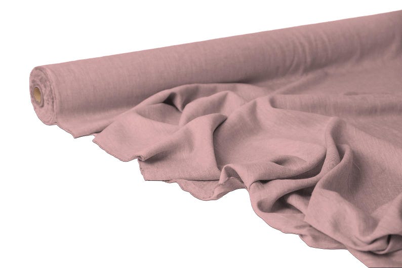 May include: A roll of dusty rose-colored fabric, partially unrolled to reveal soft folds. The fabric appears to be linen or a similar lightweight material, ideal for clothing or home decor projects. The roll is positioned on a white background.