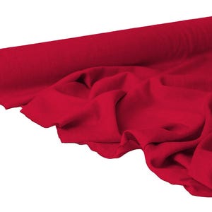 May include: A roll of vibrant red fabric, partially unrolled to reveal the texture and drape. The fabric is a solid color, with soft folds and a smooth appearance, suggesting a material suitable for clothing or home decor.