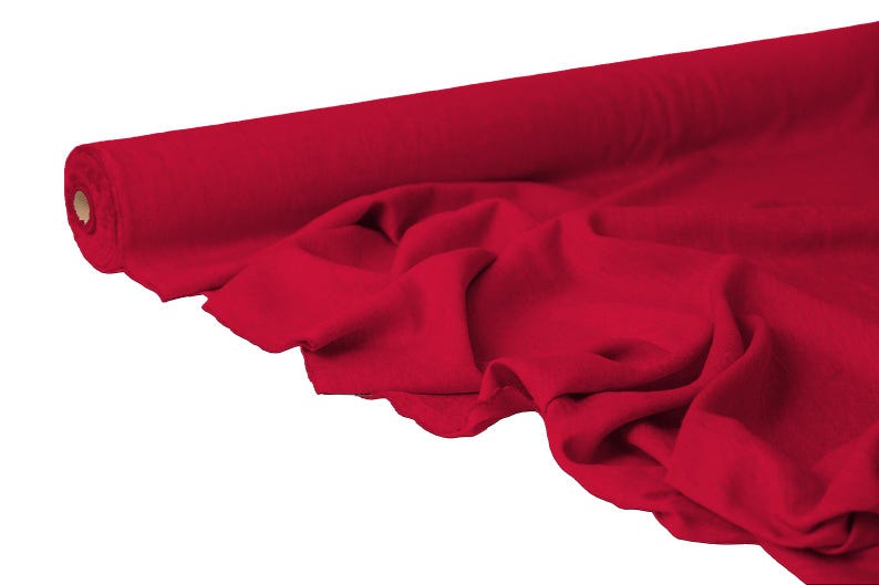 May include: A roll of vibrant red fabric, partially unrolled to reveal the texture and drape. The fabric is a solid color, with soft folds and a smooth appearance, suggesting a material suitable for clothing or home decor.