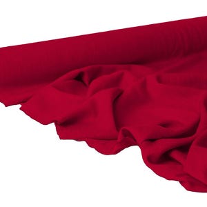 May include: A roll of vibrant red fabric, partially unrolled to reveal soft folds. The fabric is a solid, deep red color, with a smooth texture. The roll is positioned on the left, with the unrolled fabric cascading towards the right.
