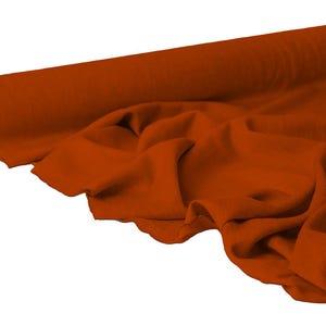 May include: A roll of rust-colored fabric, partially unrolled to reveal the soft texture. The fabric is draped in gentle folds, showcasing its flexibility and potential for various sewing projects. The color is a warm, earthy tone.