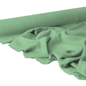 May include: A roll of sage green fabric with a soft, textured appearance. The fabric is partially unrolled, displaying its draped folds. The material appears to be lightweight and suitable for various sewing projects.