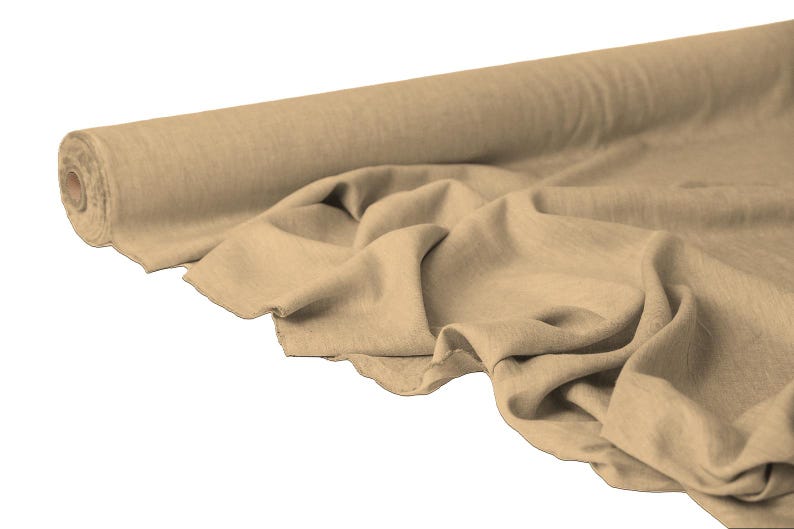 May include: A roll of beige fabric with a natural, textured appearance. The fabric is partially unrolled, displaying soft folds and a raw edge. The neutral color and texture suggest it could be used for various sewing and crafting projects.