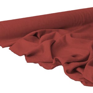 May include: A roll of red fabric, partially unrolled to reveal the texture and drape of the material. The fabric is a solid color, with a slightly wrinkled appearance, suggesting it is soft and pliable. The background is plain white.