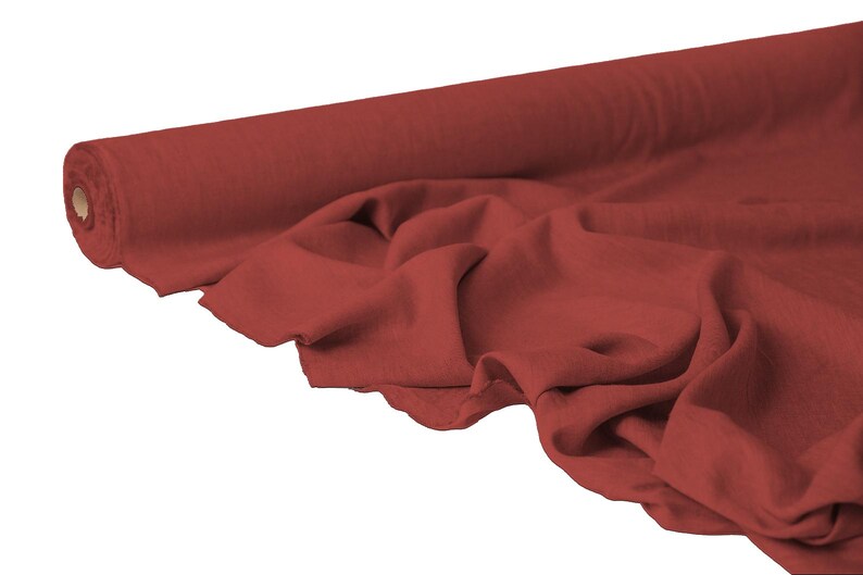 May include: A roll of red fabric, partially unrolled to reveal the texture and drape of the material. The fabric is a solid color, with a slightly wrinkled appearance, suggesting it is soft and pliable. The background is plain white.
