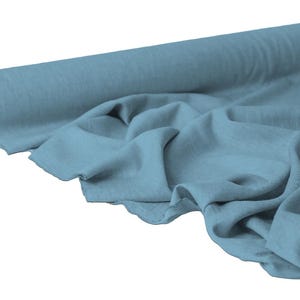 May include: A roll of light blue fabric with a soft, textured appearance. The fabric is partially unrolled, displaying its draped folds. The core of the roll is visible, showing a brown cardboard center. The fabric appears to be a lightweight material.
