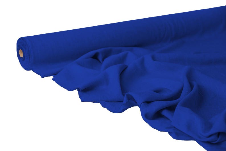 May include: A roll of vibrant blue fabric, partially unrolled to reveal soft folds. The fabric is a solid, rich blue color, and the roll's core is visible at the end. The material appears to be lightweight and suitable for various sewing projects.