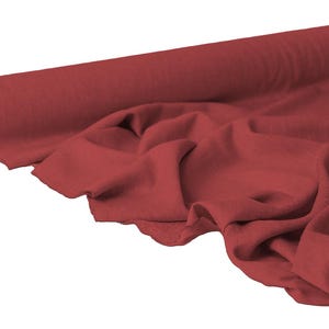 May include: A roll of red fabric with a soft, draped appearance. The fabric is a solid color and appears to be a lightweight material, suitable for various sewing and crafting projects. The fabric is unrolled, showing the texture and color.