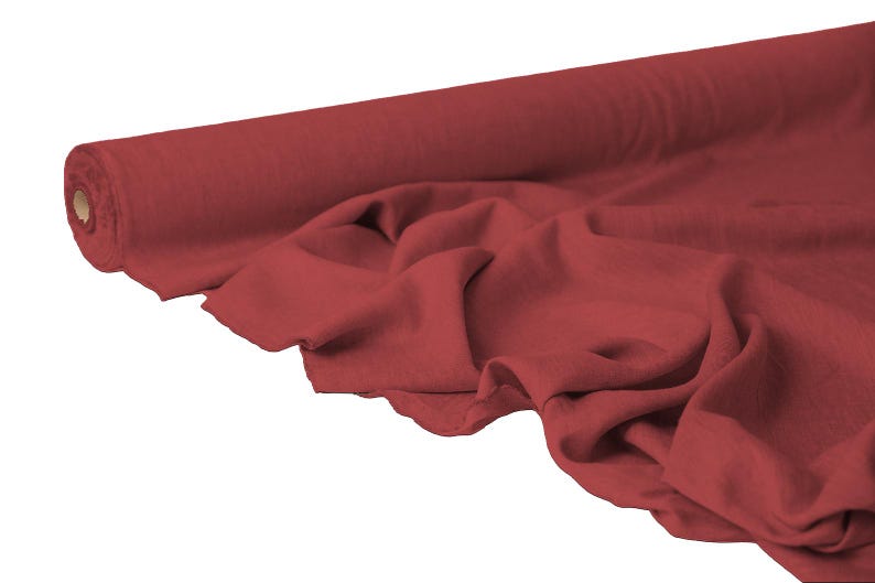 May include: A roll of red fabric with a soft, draped appearance. The fabric is a solid color and appears to be a lightweight material, suitable for various sewing and crafting projects. The fabric is unrolled, showing the texture and color.