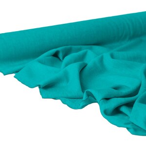 May include: A roll of turquoise fabric with a visible texture. The fabric is partially unrolled, revealing soft folds and a glimpse of the cardboard core. The color is a vibrant teal, suitable for various sewing and crafting projects.