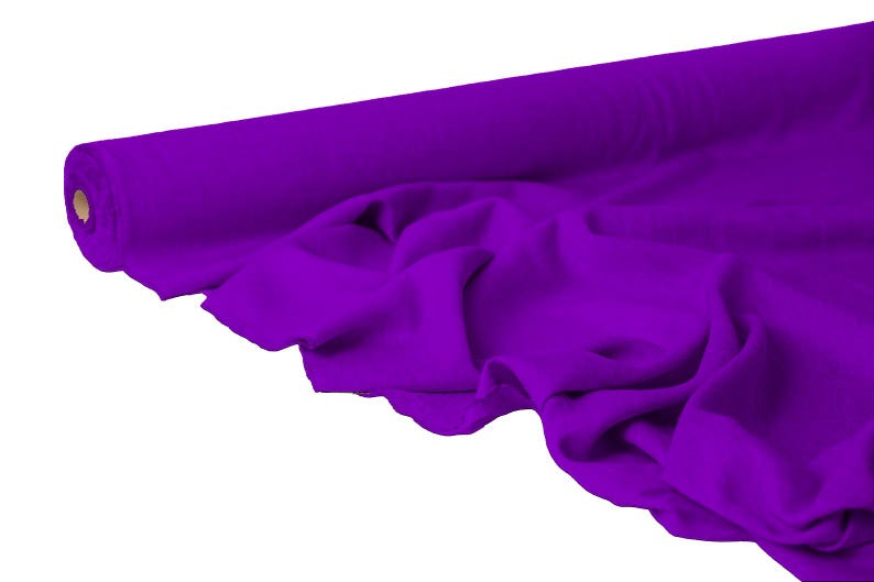 May include: A roll of vibrant purple fabric, partially unrolled to reveal soft folds. The fabric is a solid color, with a smooth texture. The roll is positioned on the left side of the image, with the unrolled fabric cascading towards the right.