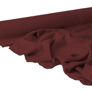 May include: A roll of burgundy fabric with a soft, draped appearance. The fabric is unrolled, revealing its texture and color. The material is likely used for sewing, crafting, or upholstery projects.