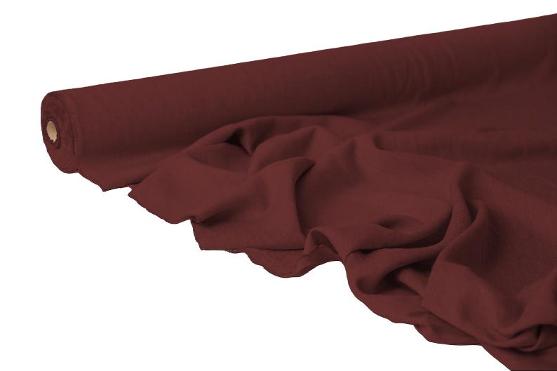May include: A roll of burgundy fabric with a soft, draped appearance. The fabric is unrolled, revealing its texture and color. The material is likely used for sewing, crafting, or upholstery projects.