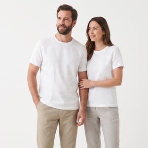 May include: Two individuals wearing plain white short-sleeved crew neck t-shirts. One individual wears tan trousers, while the other wears light grey trousers. The garments are simple, solid-coloured, and feature a standard fit with short sleeves.