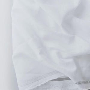 Peut inclure: Gros plan sur un tissu blanc pli&eacute;. Le tissu pr&eacute;sente une texture douce avec des plis et des froissements visibles. Les bords sont l&eacute;g&egrave;rement effiloch&eacute;s, pour un aspect simple et &eacute;pur&eacute;. Le tissu semble &ecirc;tre du coton ou du lin.