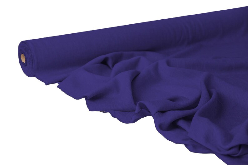 May include: A roll of deep purple fabric, partially unrolled to reveal the draped material. The fabric is a solid color, with visible folds and soft shadows, suggesting a flowing texture. The roll is cylindrical with a cardboard core.