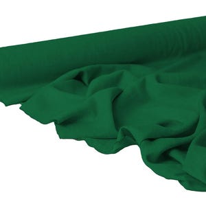 May include: A roll of emerald green fabric, partially unrolled to reveal the soft texture. The fabric is draped, showing folds and shadows, with a neutral background. The roll's core is visible, adding depth to the image.