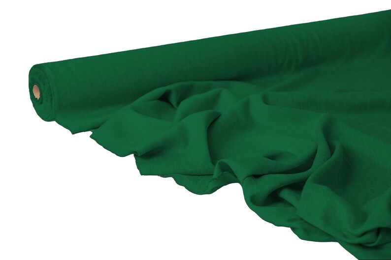 May include: A roll of emerald green fabric, partially unrolled to reveal the soft texture. The fabric is draped, showing folds and shadows, with a neutral background. The roll's core is visible, adding depth to the image.