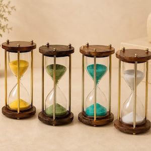 May include: Four hourglasses with wooden tops and bases, brass-colored metal supports, and clear glass chambers. Each hourglass contains a different color of sand: yellow, green, teal, and white. The hourglasses are arranged on a light-colored surface.