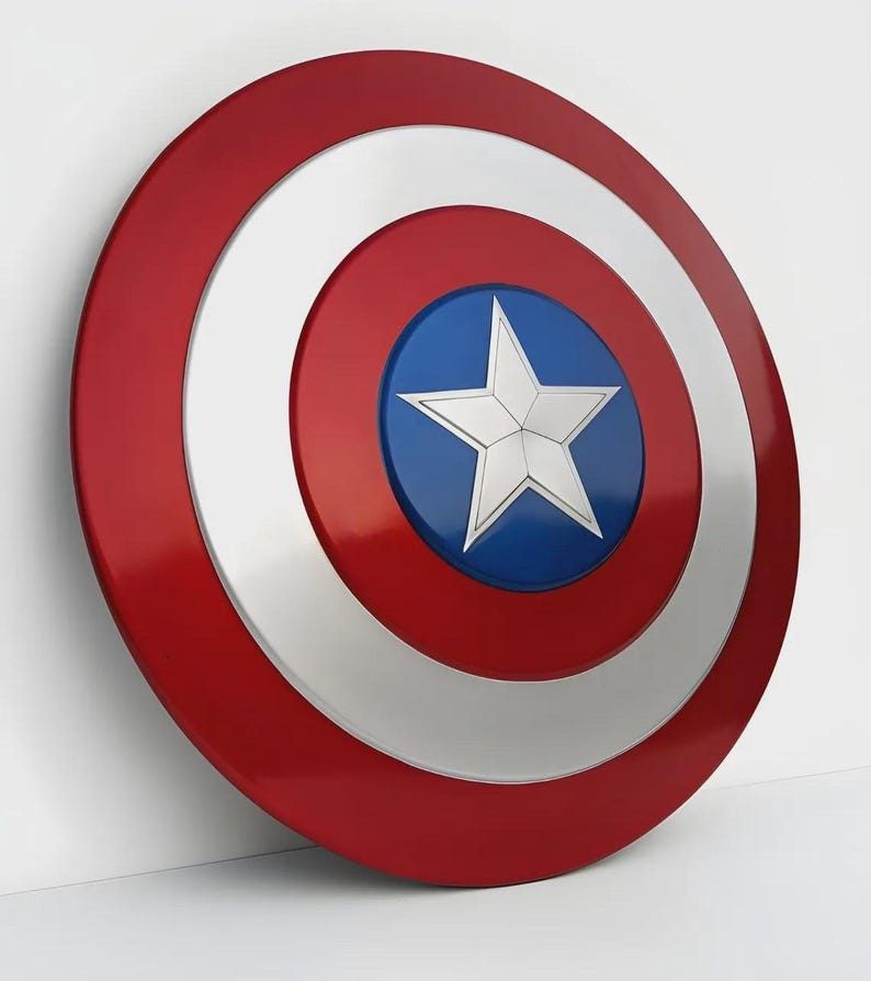 May include: A red, white, and blue shield with a star in the center. The shield has a circular design with a red outer ring, a white middle ring, and a blue center with a white star. The shield is a prop or collectible.