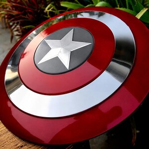 May include: A glossy, red and silver shield with a central silver star on a dark gray circle. The shield has concentric rings of red, silver, and red. A classic superhero accessory.