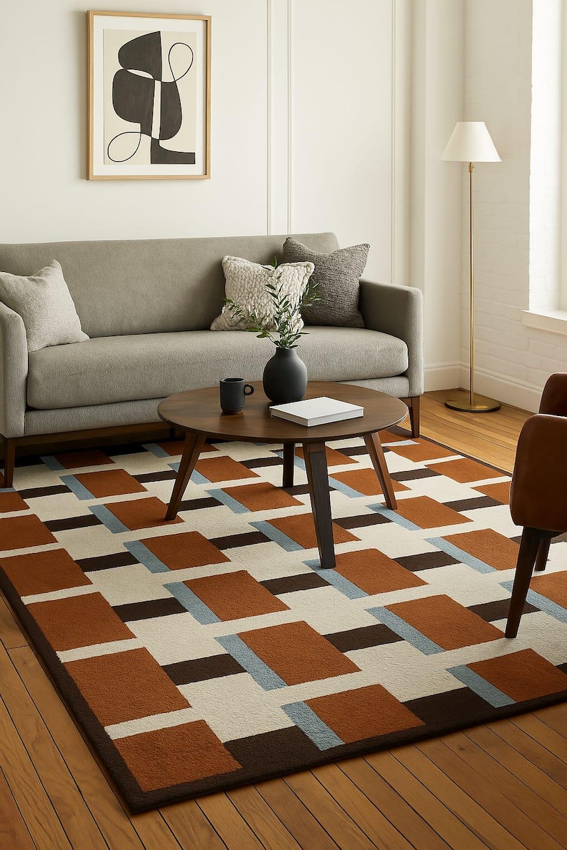 May include: A geometric patterned area rug in a living room setting. The rug features a repeating pattern of brown, light blue, and cream-colored rectangles. A gray sofa, round wooden coffee table, and artwork are also visible.