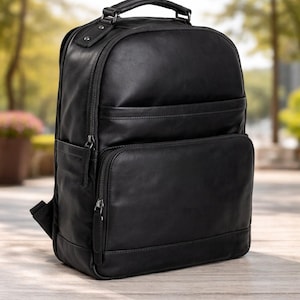 May include: Black leather backpack with multiple zippered compartments and a top handle. The backpack has a rectangular shape with a front pocket and adjustable shoulder straps. The bag is made of a smooth, matte leather material.