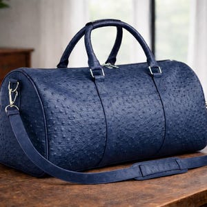 May include: A navy blue duffel bag featuring a textured ostrich-skin pattern. The bag includes two top handles, a detachable shoulder strap with a padded section, silver-toned metal hardware, and a zippered main compartment closure.