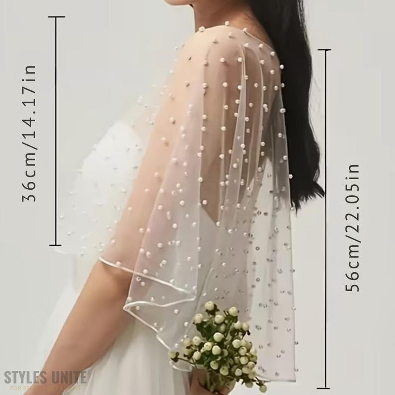 May include: A sheer, ivory-colored bridal cape, adorned with scattered pearl-like beads. The cape measures 14.17 inches (36cm) wide and 22.05 inches (56cm) long. The cape is worn over a white dress, and the bottom edge is trimmed with a delicate border.