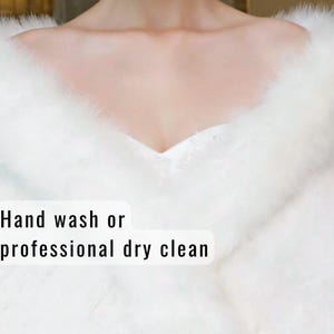 May include: A close-up of a white, fluffy, faux fur shawl or wrap. The neckline is visible, and the garment appears soft and luxurious. The text "Hand wash or professional dry clean" is displayed.