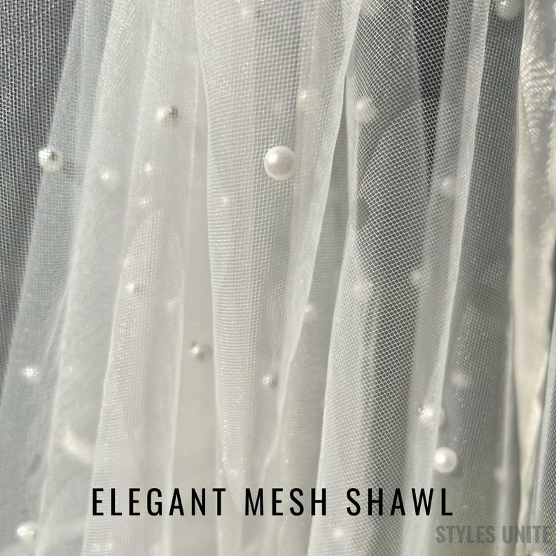 May include: White mesh shawl with scattered faux pearls. The text "ELEGANT MESH SHAWL" is displayed at the bottom of the image. The shawl is draped, creating soft folds and shadows. The overall effect is delicate and elegant.
