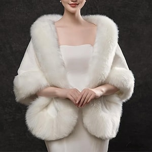May include: A white faux fur shawl with a square neckline and fluffy trim. The shawl is designed to drape over the shoulders, with a soft, luxurious appearance. The fur trim is thick and plush, adding warmth and elegance to the garment.
