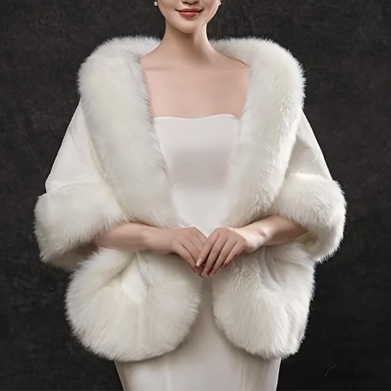May include: A white faux fur shawl with a square neckline and fluffy trim. The shawl is designed to drape over the shoulders, with a soft, luxurious appearance. The fur trim is thick and plush, adding warmth and elegance to the garment.