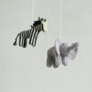 May include: A handcrafted baby mobile with two knitted animal figures. One is a grey elephant with a trunk, and the other is a zebra with black and white stripes. Both are suspended by white strings.
