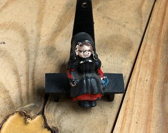 A cast iron figurine of an Amish girl sitting on a bench hook